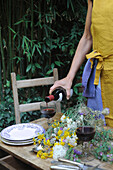 Frau serviert ein Glas Rotwein auf Holztisch im Garten