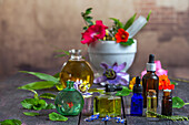 Various essential oils in vials surrounded by medicinal plants and flowers