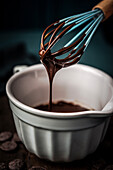 Whisk and small bowl with chocolate sauce