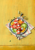 Salat aus bunten Tomaten mit Mini-Mozzarella und Erdbeeren auf gelbem Untergrund