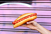 Hand held hot dog with frankfurter sausage and ketchup