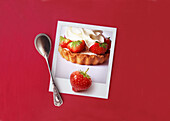 Polaroid-Foto von Erdbeertörtcheen darauf Erdbeere vor rotem Hintergrund