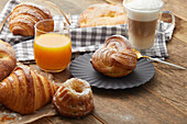 Coffee with foamy milk,orange juice and an assortment of milkbread pastries for breakfast