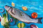 Raw sea bass on a blue background surrounded by vegetables