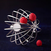 Whisk with raspberries against a black background (Close Up)
