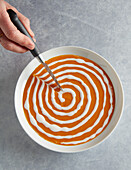 Decorating the soup by feathering the crema drawing the knife from the center towards the edge of the bowl