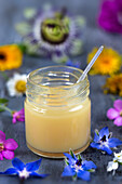 Gelée royale en gros plan avec sa cuillère remplie, sur un fond foncé vertical parsemé de fleurs.