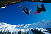 Couple jumping from roof of apine hut