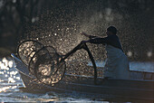 Fisherman throwing net into water, Chiemsee, Bavaria, Germany