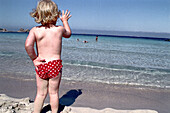 Kleines Kind steht am Strand in der Sonne, Sardinien, Italien