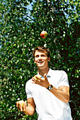 Mann jongliert mit Aepfeln
