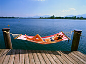 Woman lying on hammock by a lake, Upper Bavaria, Germany