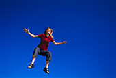 Woman jumping up in front of cloudless sky