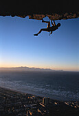Rock climber climbing an overhang, Muizenberg Bay, South Africa