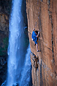 Man climbing a steep rock face near a waterfall, Waterval Boven, South Africa