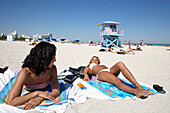 Zwei junge Frauen liegen in der Sonne, Strandleben, South Beach, Miami, Florida, USA