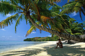 A woman sitting on the beach in the shade, Ile aux Nattes, Ste Marie, Madagascar, Indian Ocean