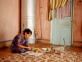Woman cutting vegetables in front of curious cat, Uzbekistan