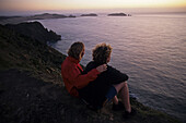 Couple watching sunset at Cape Reinga, northernmost point of New Zealand, North Island, New Zealand
