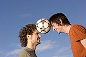 Two young man juggling soccer ball between their heads