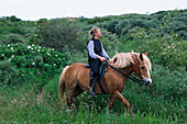 Frau reitet mit Pferd durch die Dünen, Niedersachsen, Deutschland