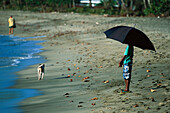 Junge mit Sonnenschirm am Strand, Tobago West Indies, Karibik