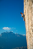 A woman climbing up a rock face in front of blue sky