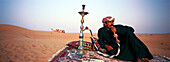 Beduine raucht Wasserpfeife in der Wüste, Dubai, Vereinigte Arabische Emirate