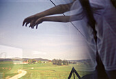 Nicht erkennbarer Mensch greift nach Landschaft, halb gespiegelt in Zugfenster, Allgäu, Bayern, Deutschland