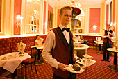 Waiter serving Sachertorte in restaurant Anna Sacher of Hotel Sacher, Vienna, Austria