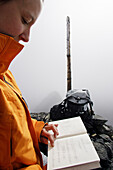 Woman reads summit book on a misty mountain summit, Piz Quattervals, Swiss National Park, Engadin, Graubuenden, Grisons, Switzerland, Alps