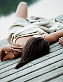Young woman lying on jetty, covered with blanket