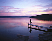 Adult and child standing on jetty, sunset