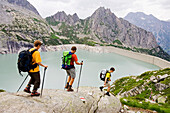 Drei Wanderer wandern über einen felsigen Weg hinunter zum Albigna Stausee. Albigna Stausee, Bergell, Graubünden, Graubuenden, Schweiz, Alpen.