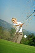 Junge Frau mit blonden Haaren beim Golfen am Abschlag auf einem Golfplatz