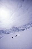 Four people with skies and snowboard walking up a snowcapped mountain, Kuehtai, Tyrol, Austria