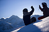 Junge Frau und Mann sitzen im Schnee, klatschen sich ab, Kühtai, Tirol, Österreich