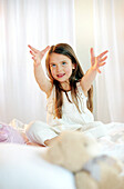 Girl sitting on bed, arms outstretched