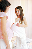 Mädchen stösst mit ihrem Bauch an schwangere Mutter