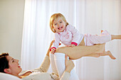 Toddler girl balancing on mother's knees on bed, side view