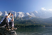 Man looking with binocular over Lake, Eibsee, Zugspitze in backround, Bavaria Germany