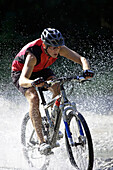 Mountainbiker fährt durch Wasser, Oberammergau, Deutschland