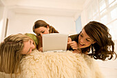 Teenage girls (14-16) on bed with laptop