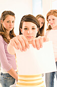 Teenage girl (14-16) tearing a paper, three girls standing around