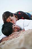 Couple in clothes lying on beach, woman kissing man' s neck