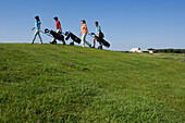 Group of people walking on golf course pulling golf bag on wheels, sideview, Apulia, Italy