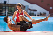 Female trainer helping man with stretching exercises, poolside, Apulia, Italy