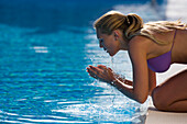 Junge Frau erfrischt Gesicht am Pool, Apulien, Italien