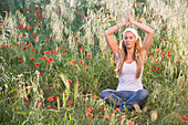 Young woman meditating on meadow with poppy flowers, Apulia, Italy