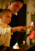 Girl (3-4 years) light up a candle on christmas tree